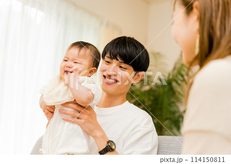 泣く赤ちゃんを抱っこしながらあやす父親とそれを見守る母親の3人家族 114150811