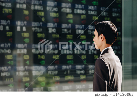 ビジネス街の株価ボードを見てNISAでの運用を考える30代の日本人のビジネスマンの男性の横顔 114150863