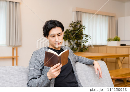 自宅のリビングで休日の趣味の読書を楽しむ30代の男性 114150938