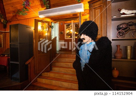 A man with a beard and mustache is wearing a fur coat and hat. He is standing in a restaurant with a rustic interior. 114152904