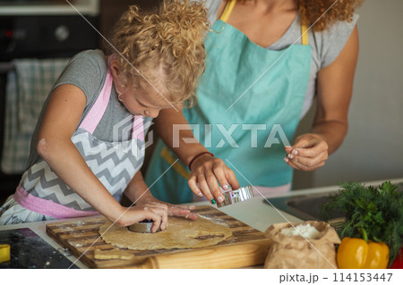 Beautiful young mom and her cute little daughter rolling out dough at home. Beautiful young mom and her cute little daughter rolling out dough at home. 114153447