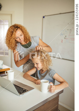Smiling Mother helps her adorable daughter with homework at living room 114153496