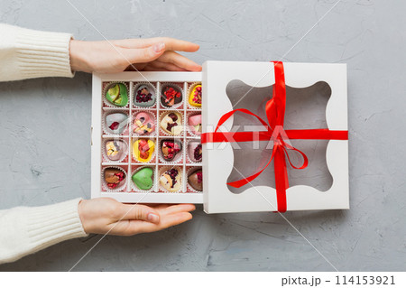 Female hands with delicious candies in box on color background 114153921