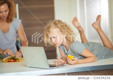 Little girl and her daughter baking cookies at home, reading recipe on laptop. 114154258