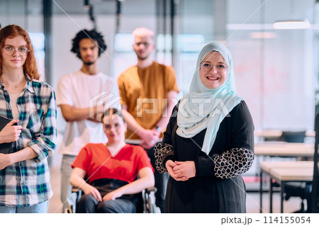 A diverse group of young business people walking a corridor in the glass-enclosed office of a modern startup, including a person in a wheelchair and a woman wearing a hijab A diverse group of young business people walking a corridor in the glass-enclosed office of a modern startup, including a person in a wheelchair and a woman wearing a hijab 114155054