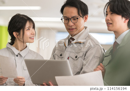 打ち合わせをする男女3人の作業着姿のエンジニア 打ち合わせをする男女3人の作業着姿のエンジニア 114156194