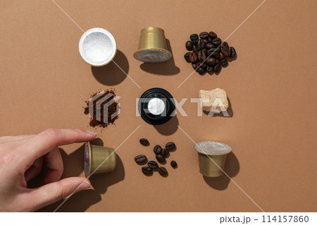 Coffee capsules, coffee beans, sugar and hand on brown background, top view 114157860