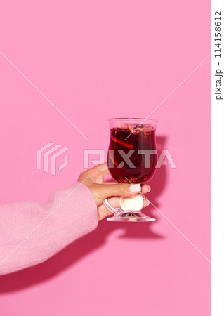 Glass with mulled wine made with red wine and cinnamon against pink background. Traditional winter drink Glass with mulled wine made with red wine and cinnamon against pink background. Traditional winter drink 114158612