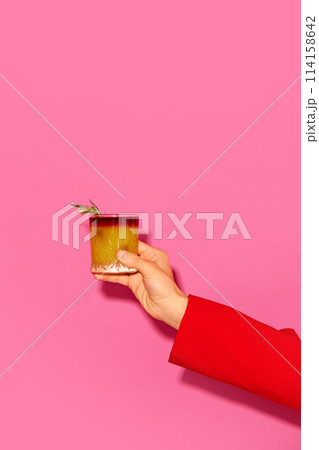 Female hand holding cocktail with orange juice against pink background. New York sour traditional cocktail Female hand holding cocktail with orange juice against pink background. New York sour traditional cocktail 114158642