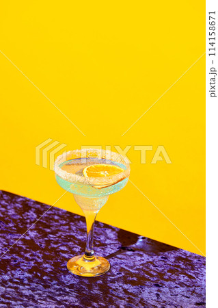 Sweet and sour margarita cocktail with slice of orange against vivid yellow background 114158671