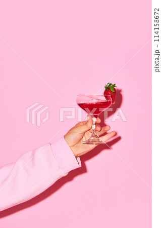 Male hand holding sweet cocktail with strawberry and coconut against pink background. Relaxation 114158672