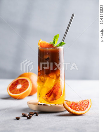 Espresso coffee with orange juice (bumble) in a tall glass with ice and mint on a blue background Espresso coffee with orange juice (bumble) in a tall glass with ice and mint on a blue background 114158822