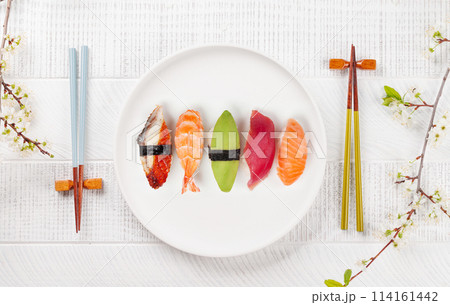 Sushi plate adorned with cherry blossom branch and chopsticks, epitomizing Japanese food culture 114161442
