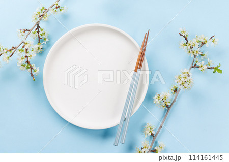 Table adorned with cherry blossom branch and chopsticks, epitomizing Japanese food culture Table adorned with cherry blossom branch and chopsticks, epitomizing Japanese food culture 114161445