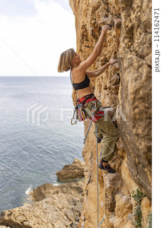 A woman is climbing a rock wall while wearing a black tank top and red 114162471