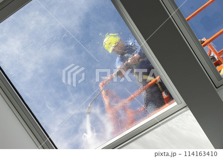 Worker on a cherry picker cleaning a roof windows with high pressure water jet. Low angle shot 114163410