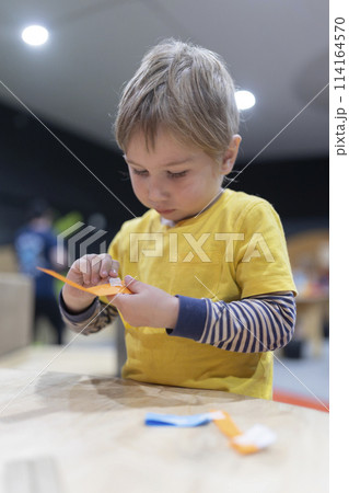 A young boy is sitting at a table, cutting paper with scissors 114164570