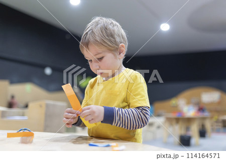 A young boy is sitting at a table with a piece of paper in his hand A young boy is sitting at a table with a piece of paper in his hand 114164571