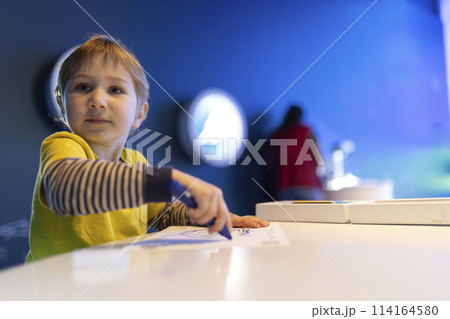 A young boy is sitting at a table with a blue marker in his hand 114164580