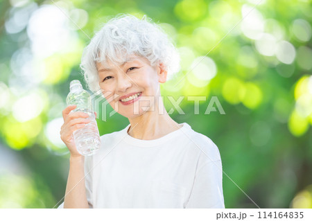 新緑の公園で水を飲むシニア女性 114164835