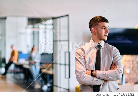 A young business leader stands with crossed arms in a modern office hallway, radiating confidence and a sense of purpose, embodying a dynamic and inspirational presence A young business leader stands with crossed arms in a modern office hallway, radiating confidence and a sense of purpose, embodying a dynamic and inspirational presence 114165182