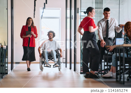 A business leader with her colleague, an African-American businessman who is a disabled person, pass by their colleagues who work in modern offices A business leader with her colleague, an African-American businessman who is a disabled person, pass by their colleagues who work in modern offices 114165274