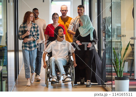 A diverse group of young business people congregates within a modern startup's glass-enclosed office, featuring inclusivity with a person in a wheelchair, an African American young man, and a hijab A diverse group of young business people congregates within a modern startup's glass-enclosed office, featuring inclusivity with a person in a wheelchair, an African American young man, and a hijab 114165511