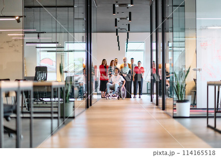 A diverse group of young business people walking a corridor in the glass-enclosed office of a modern startup, including a person in a wheelchair and a woman wearing a hijab A diverse group of young business people walking a corridor in the glass-enclosed office of a modern startup, including a person in a wheelchair and a woman wearing a hijab 114165518