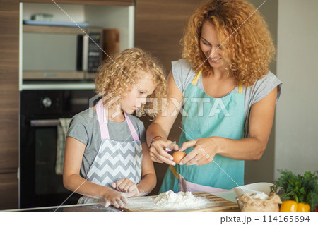 Woman and cute daughter cooking on kitchen, making dough for birthday party. Woman and cute daughter cooking on kitchen, making dough for birthday party. 114165694