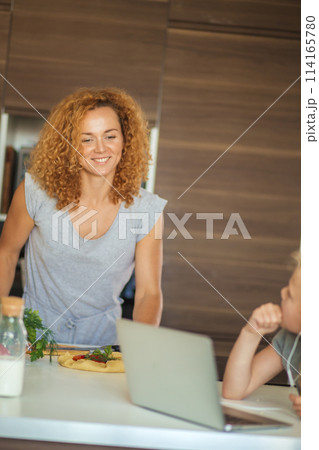 Little girl and her daughter baking cookies at home, reading recipe on laptop. 114165780