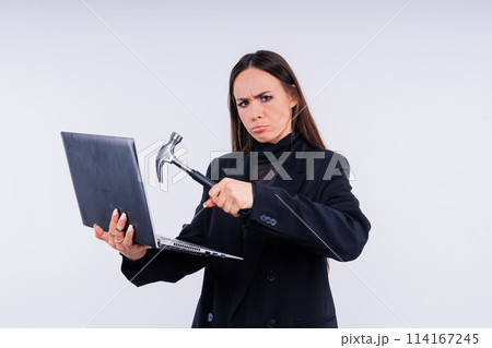 Attractive woman wearing business suit with computer angry facial expression holding a hammer Attractive woman wearing business suit with computer angry facial expression holding a hammer 114167245