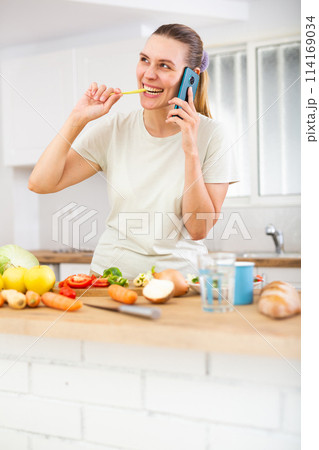 Emotional young woman standing in home kitchen and chatting on phone 114169034