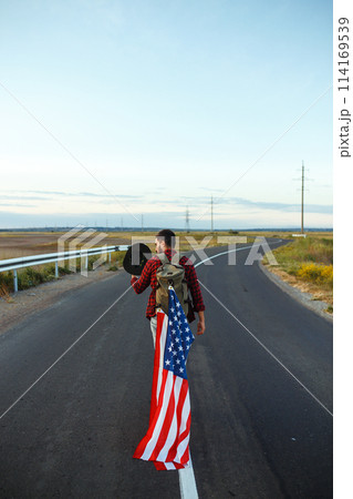 4th of July. American Flag. Traveler with the flag of America. The man in a hat, a backpack, a shirt and jeans. 4th of July. American Flag. Traveler with the flag of America. The man in a hat, a backpack, a shirt and jeans. 114169539