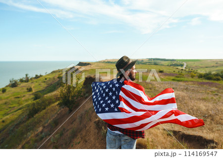 4th of July. American Flag. Traveler with the flag of America. The man in a hat, a backpack, a shirt and jeans. 4th of July. American Flag. Traveler with the flag of America. The man in a hat, a backpack, a shirt and jeans. 114169547