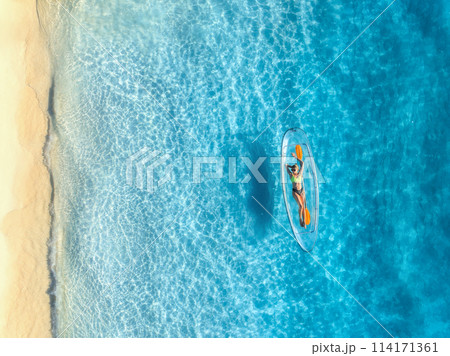 Aerial view of young woman lying on transparent canoe in blue se Aerial view of young woman lying on transparent canoe in blue se 114171361
