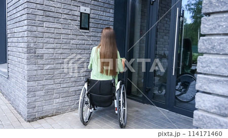 A woman in a wheelchair with an assistive device for manual control enters the entrance. Electric hand bike. 114171460