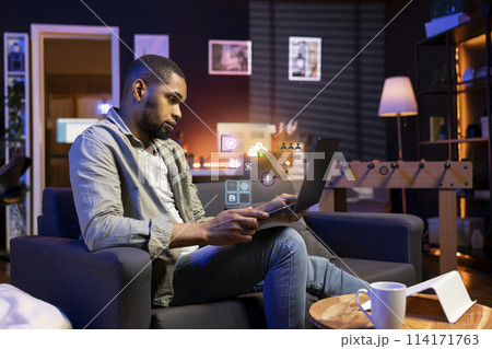 African american man working from home on laptop, solving tasks, online connectivity concept. Remote employee using AR technology to interact with notebook programs software African american man working from home on laptop, solving tasks, online connectivity concept. Remote employee using AR technology to interact with notebook programs software 114171763