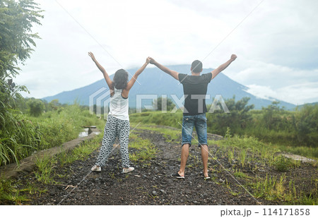 A young, happy couple in love poses in rice fields against the backdrop of Mount Agung volcano on the popular tourist island of Bali. A young, happy couple in love poses in rice fields against the backdrop of Mount Agung volcano on the popular tourist island of Bali. 114171858