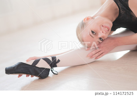 A young woman lies bent over on her feet in a ballet class. Ballerina stretches on the floor. A young woman lies bent over on her feet in a ballet class. Ballerina stretches on the floor. 114172525