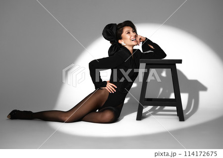 Beautiful woman in retro style in a black bodysuit and a bow in her hair in full length posing on a gray background. Beauty of body and face 114172675
