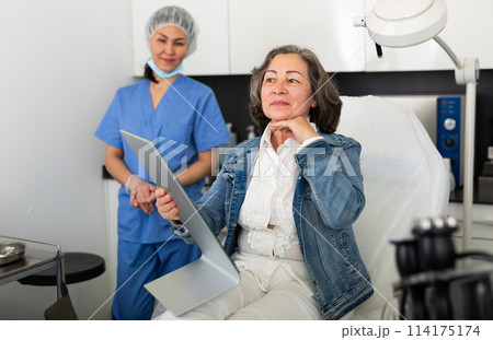 Smiling aged woman looking at mirror after hardware facial procedure Smiling aged woman looking at mirror after hardware facial procedure 114175174