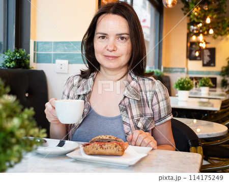 Woman having breakfast in cafe with sandwich and coffee Woman having breakfast in cafe with sandwich and coffee 114175249