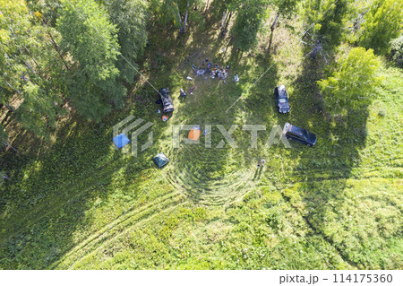 Aerial view of a tourist camp in the forest in summer, with tents and a campfire Aerial view of a tourist camp in the forest in summer, with tents and a campfire 114175360