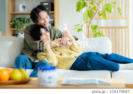 リビングでくつろぎながらスマホを見るカップル リビングでくつろぎながらスマホを見るカップル 114179087