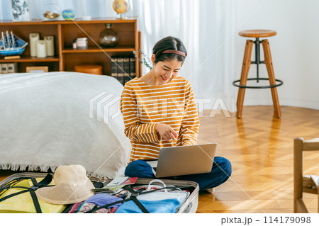 旅行の準備をしながらウェブで予約する若い女性 114179098