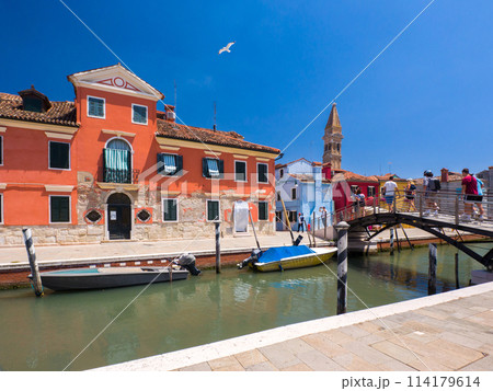 遠くに尖塔を望む水路沿いにカラフルな建物が並ぶ町 (イタリア、ブラーノ島) 遠くに尖塔を望む水路沿いにカラフルな建物が並ぶ町 (イタリア、ブラーノ島) 114179614