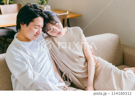 家のリビングでソファーに座る仲良しな若いアジア人夫婦 114180312