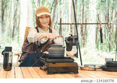 キャンプでコンロとケトルを使ってお湯を沸かしコーヒーを淹れる女性キャンパー 114180776