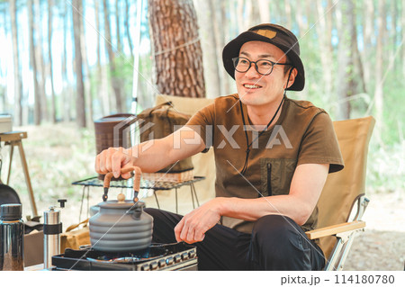 キャンプでコンロとケトルを使ってお湯を沸かしコーヒーを淹れる男性キャンパー 114180780