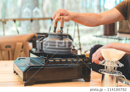 キャンプでコンロとケトルを使ってお湯を沸かしコーヒーを淹れる男性キャンパーの手元 114180782